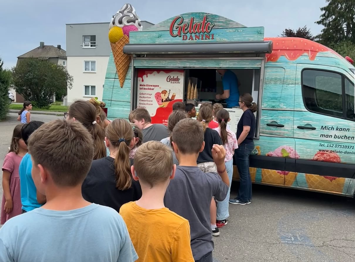 Kinder stehen in einer Schlange vor dem Gelato Danini Eiswagen und warten auf ihr Eis beim Schulfest.