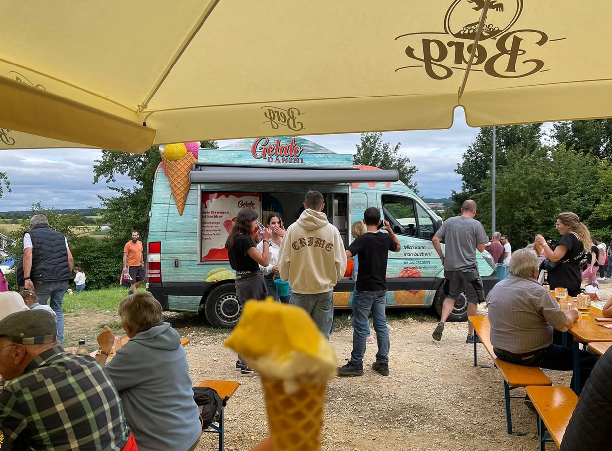 Gelato Danini Foodtruck steht auf einem Sommerfest, Gäste sitzen an Biertischen und genießen Eis und Getränke.