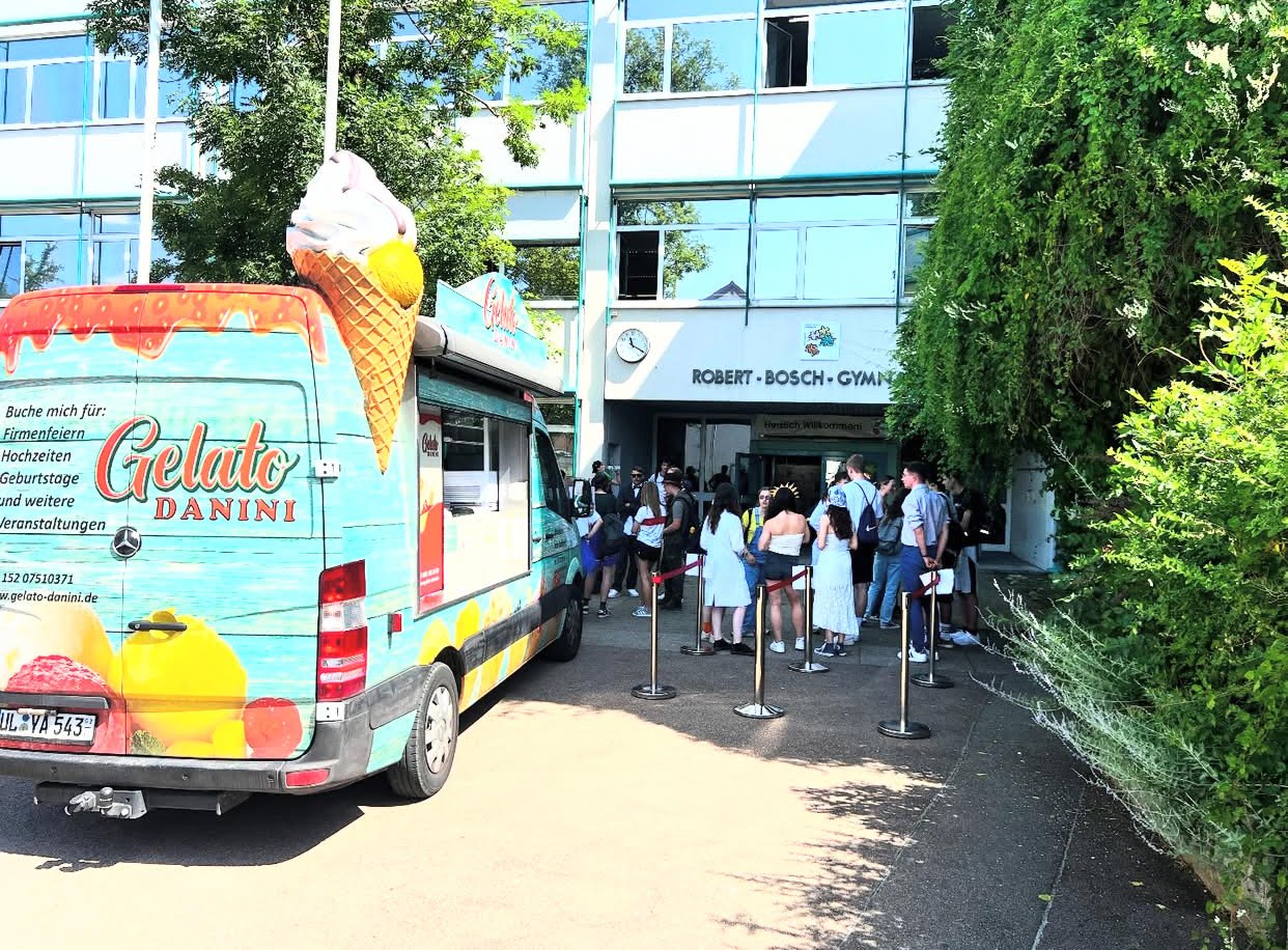 Gelato Danini Foodtruck steht vor einem Schulgebäude, Schüler warten in einer Schlange auf Eis und Süßspeisen.